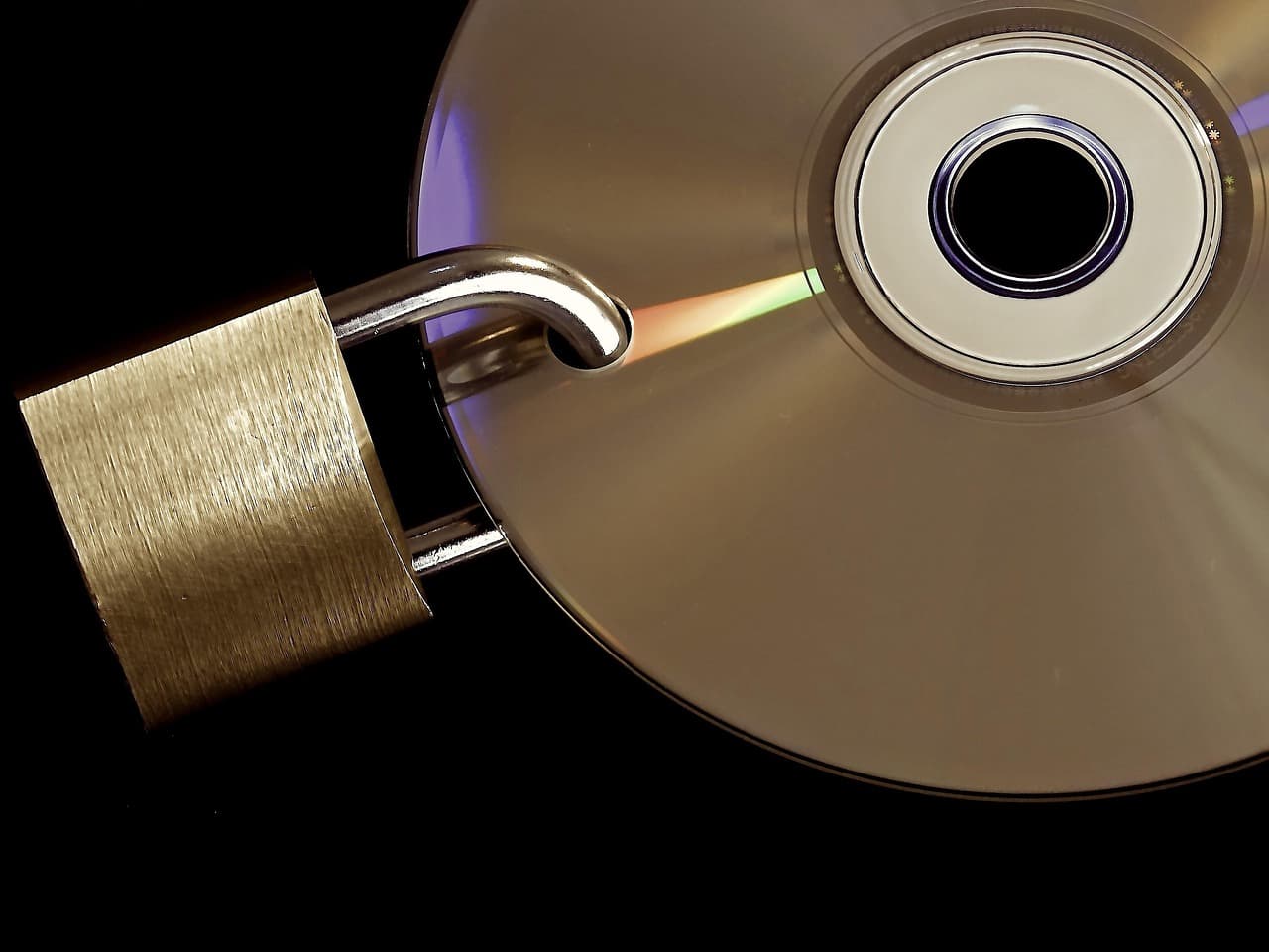 A brass padlock clamped onto a shiny optical disc against a black background, illustrating secured data storage