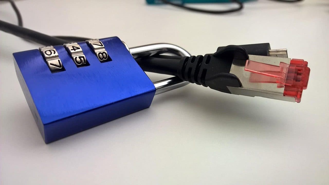 Un cadenas à combinaison bleu accroché à un câble réseau Ethernet sur un bureau