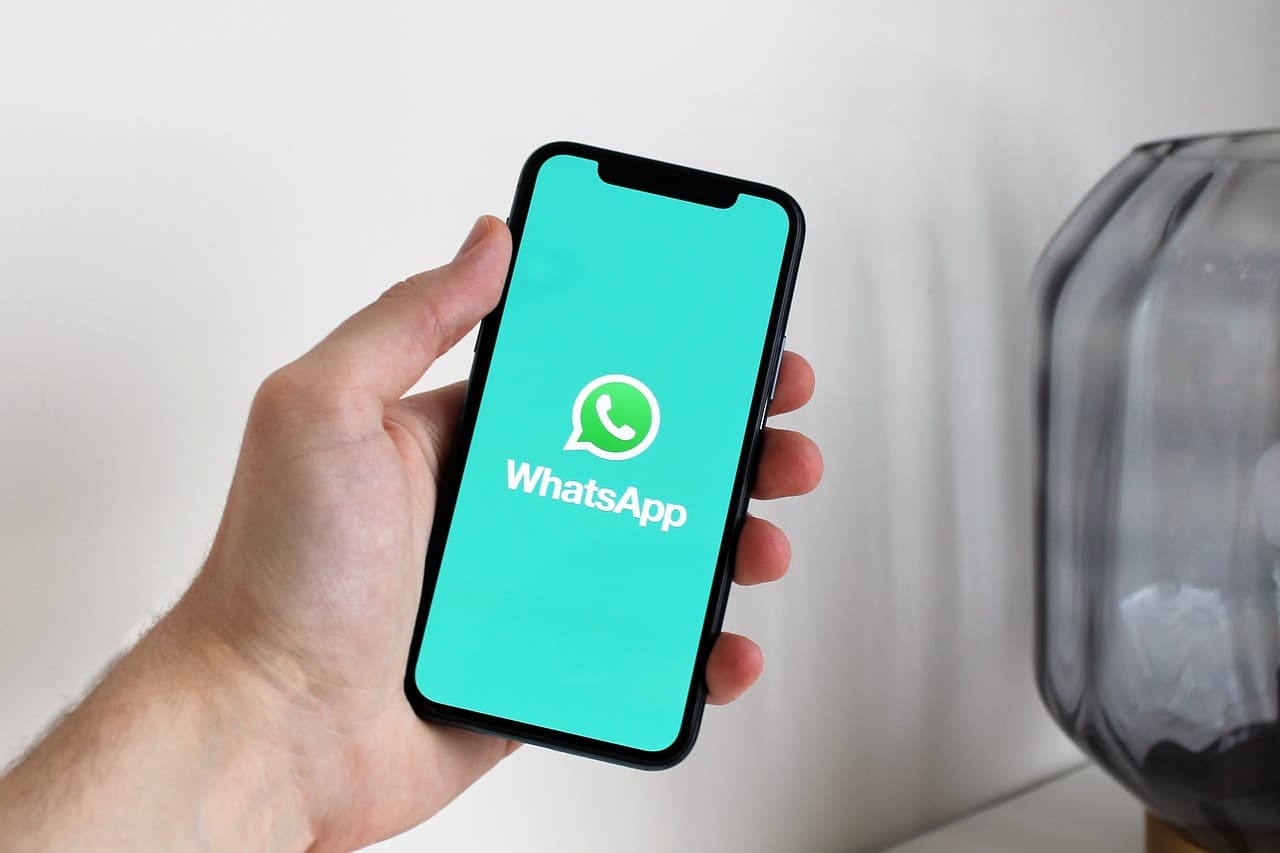 Uma mão segurando um smartphone exibindo a aplicação de mensagens WhatsApp