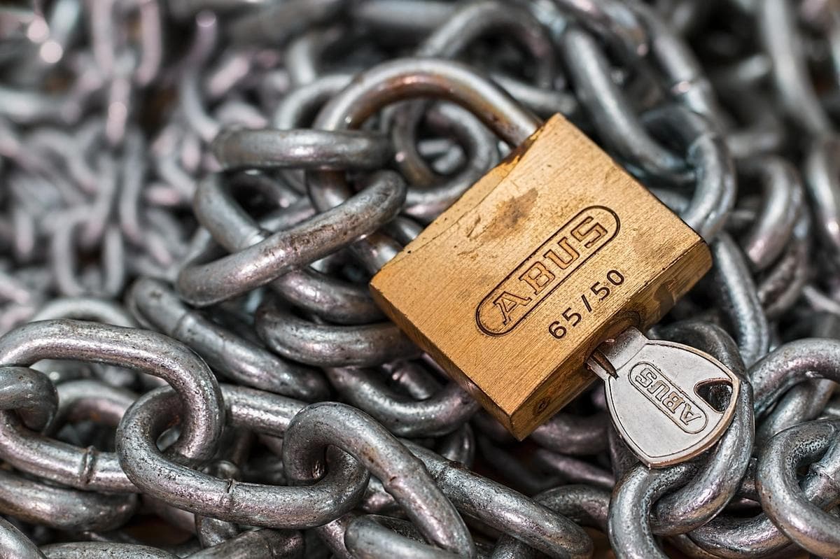 Un cadenas en laiton avec sa clé insérée, posé sur un tas de chaîne métallique — en chiffrement zero-knowledge, vous seul détenez la clé.